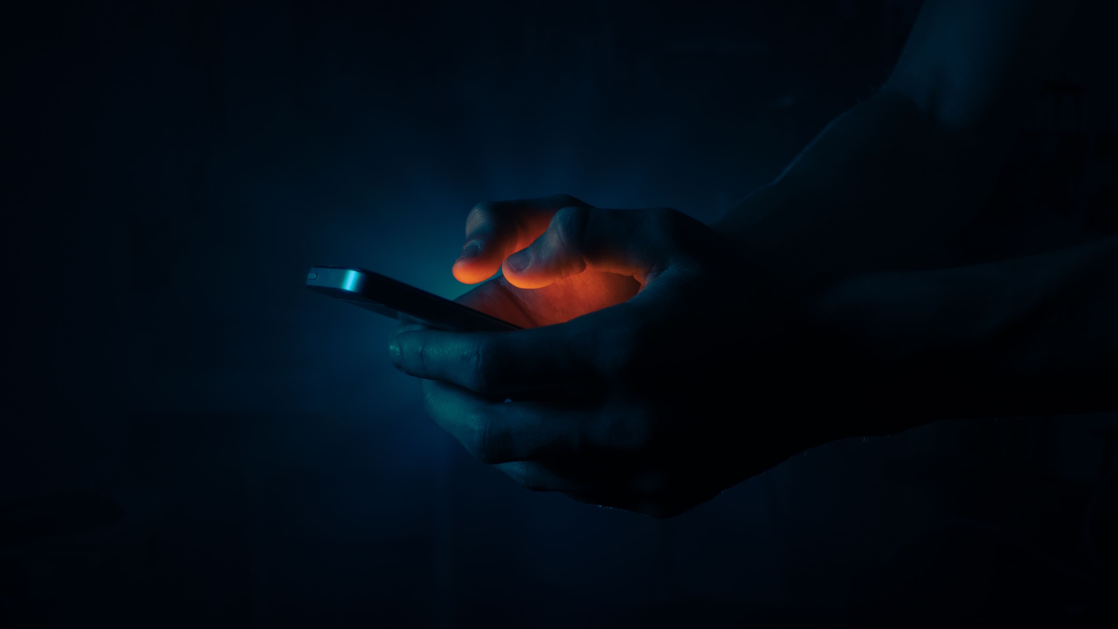 Hands holding a phone in the dark, screen glowing